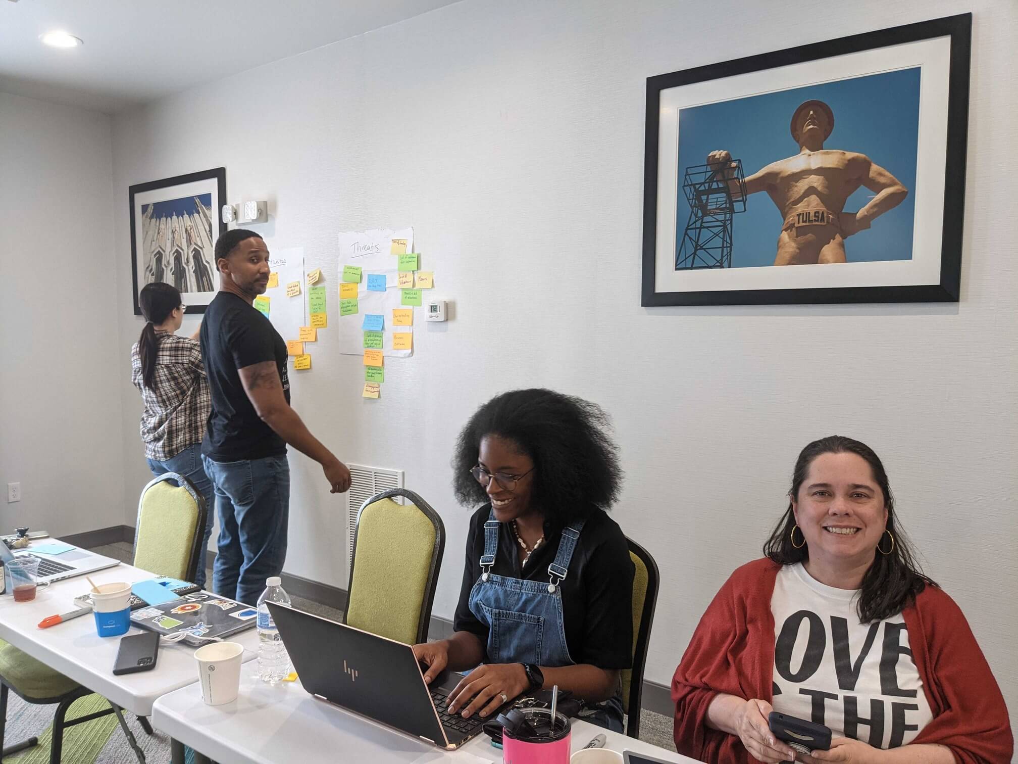 Four people in a coworking space talking to each other and adding sticky notes to the wall.